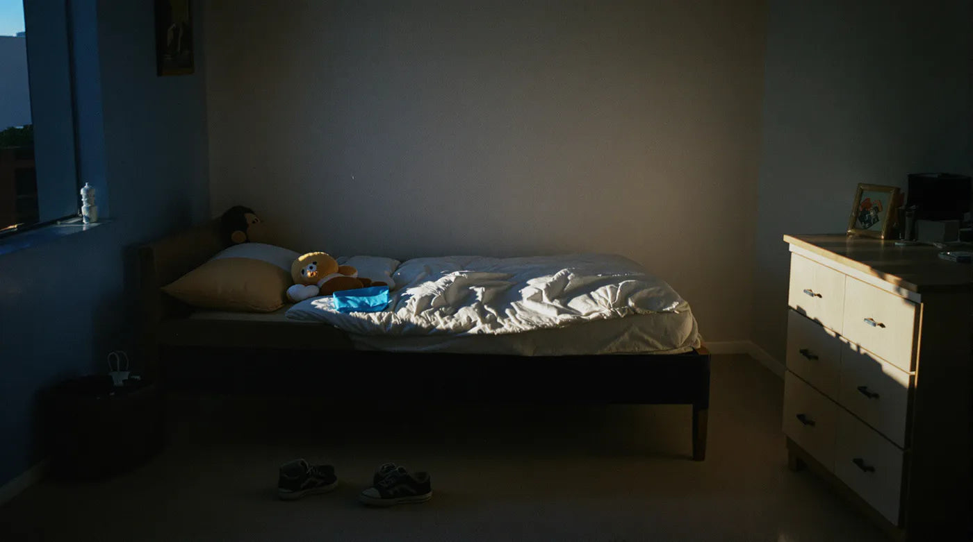 A boy's empty bedroom in early morning light, a teddy bear on the bed and small sneakers on the floor.